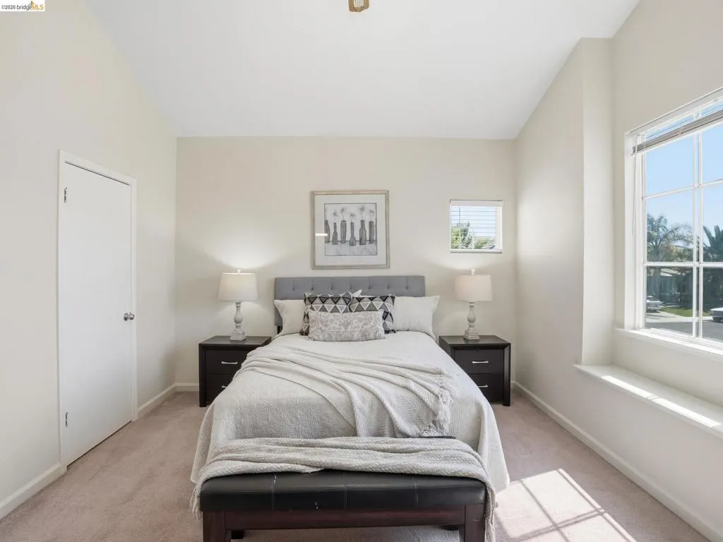 Neutral-toned room featuring a large multi-pane window with a deep sill, vaulted ceilings, and plush carpeting