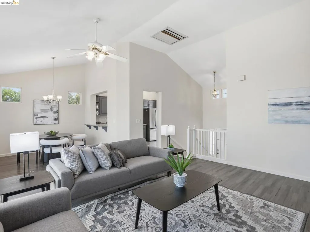 Spacious living area featuring vaulted ceilings, wood-finish flooring, a ceiling fan with integrated lighting, and an open concept layout
