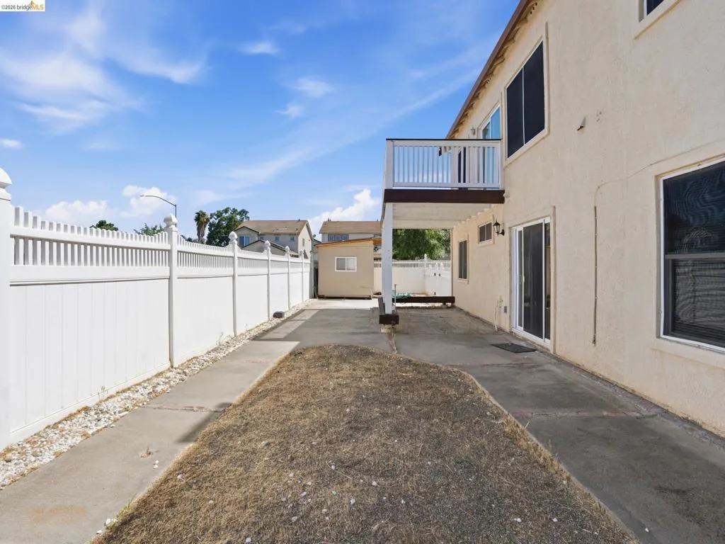 Rear exterior featuring a second-story balcony with white railings, a concrete patio, and a white picket fence