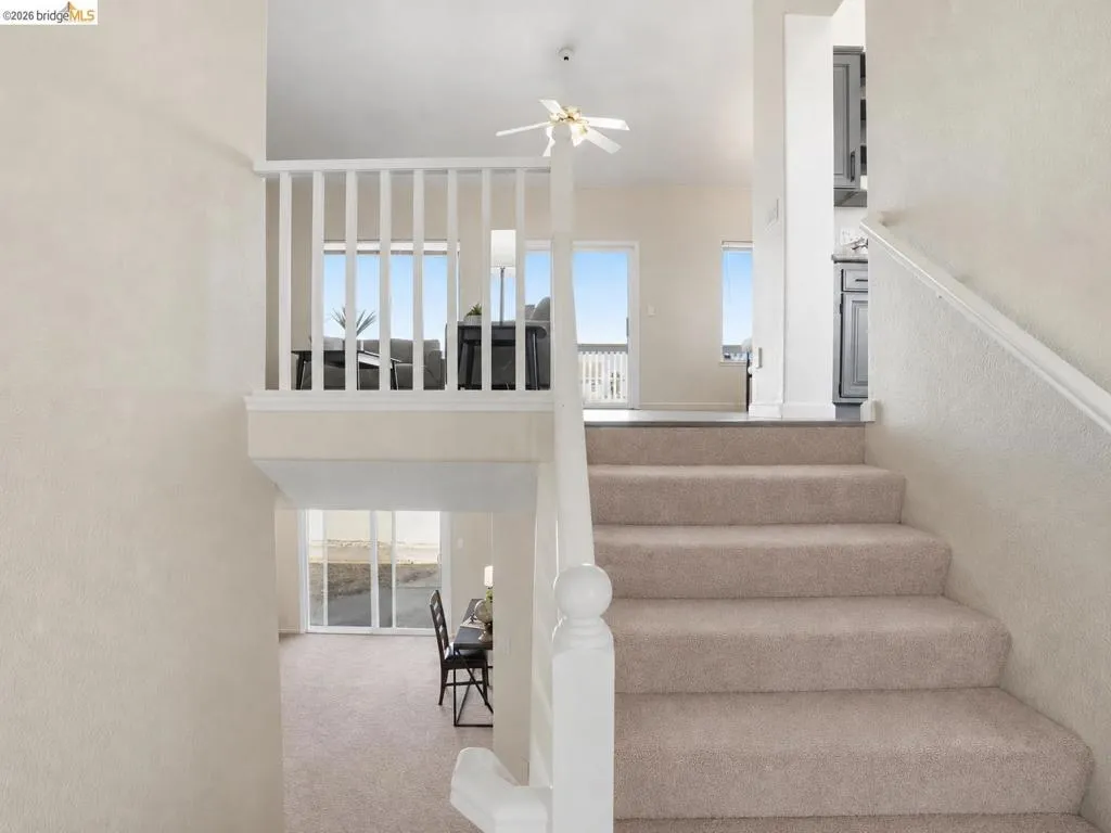 Carpeted staircase with white balustrade leading to an upper landing featuring a ceiling fan