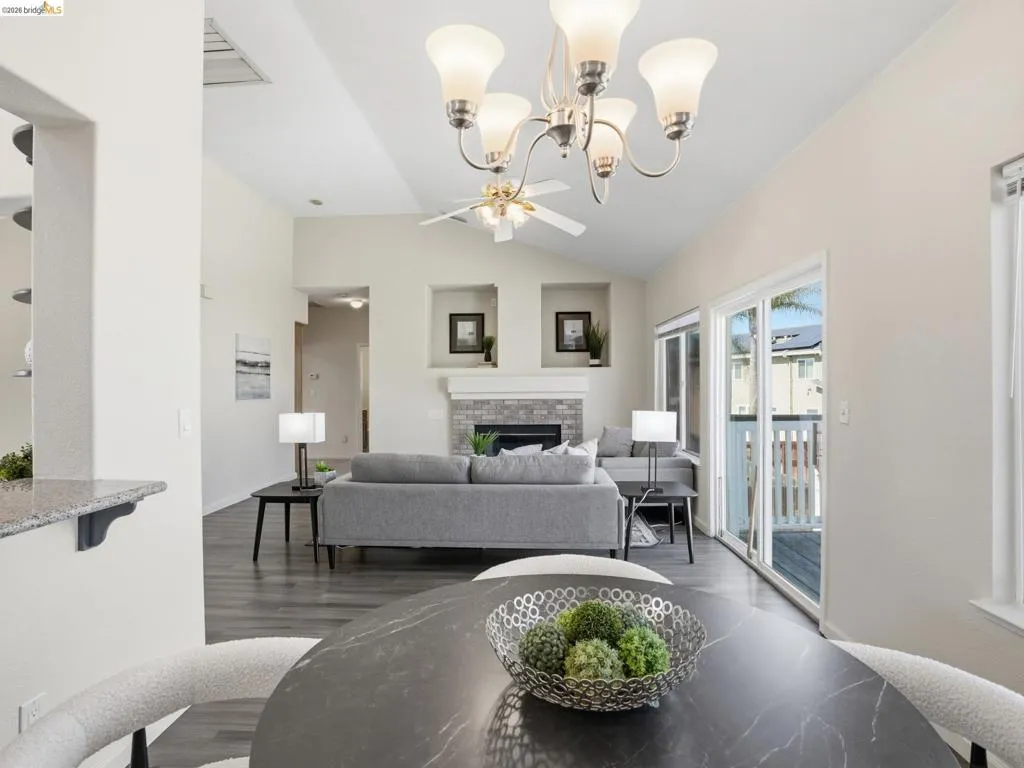 Open concept living space featuring vaulted ceilings, wood-finish flooring, a fireplace with a stone surround and mantel, and sliding glass doors to outdoor space