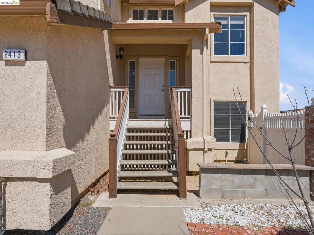 Stucco exterior with a covered entry, wood-finish railings, and a contrasting white picket fence