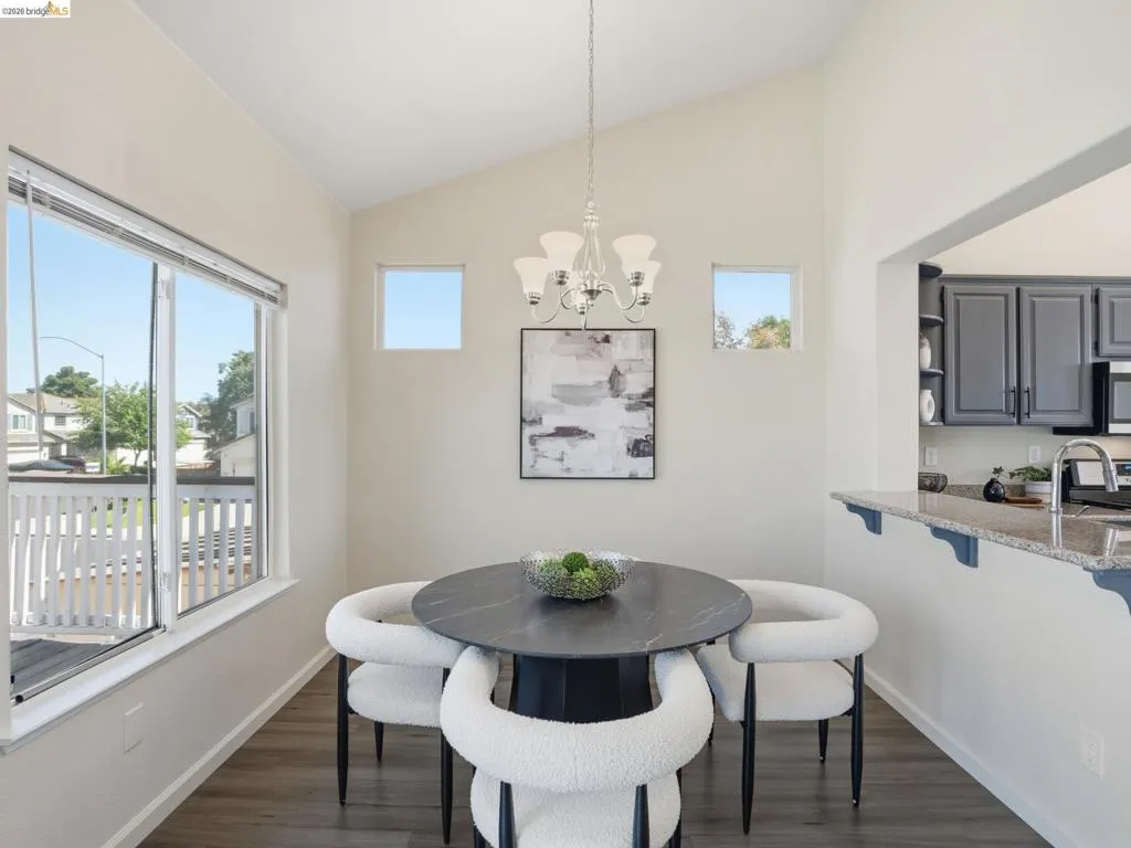 Vaulted ceiling with an elegant chandelier illuminates the dining area, complemented by wood-finish flooring