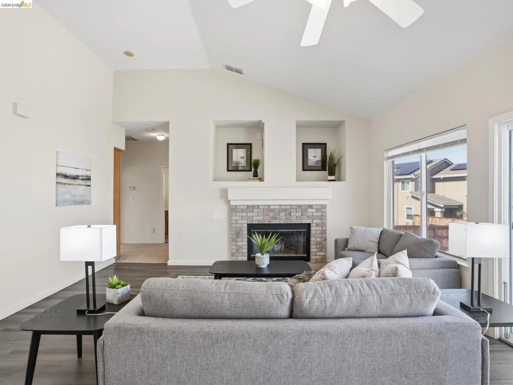Living room featuring vaulted ceilings, wood-finish flooring, and a fireplace with a light-colored brick surround and mantel