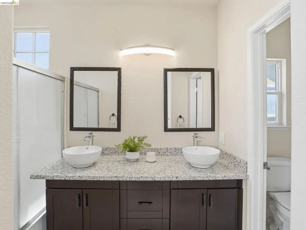 Double vanity featuring granite-look countertops, vessel sinks, and dark wood-finish cabinetry