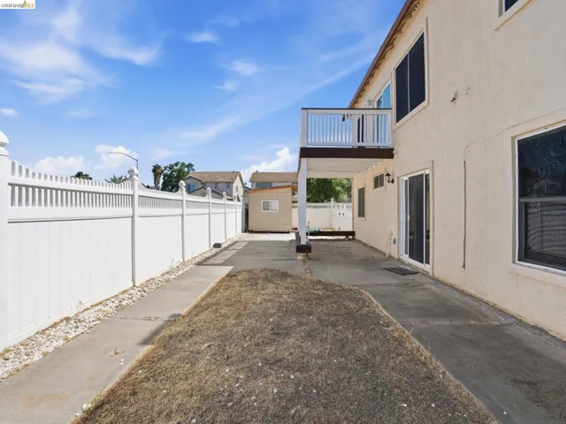 Rear exterior featuring a second-story balcony with white railings, a concrete patio, and a white picket fence