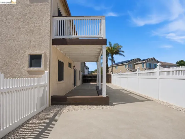 Exterior stucco wall with an upper-level balcony, covered patio, and concrete hardscaping