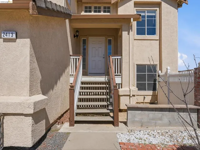 Stucco exterior with a covered entry, wood-finish railings, and a contrasting white picket fence