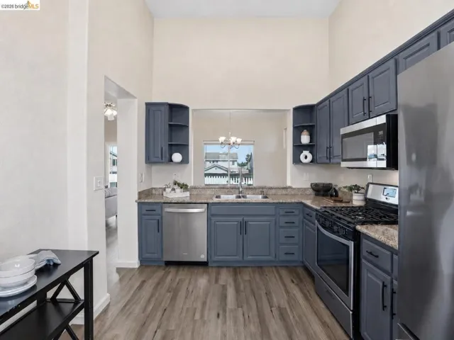 Kitchen featuring vaulted ceilings, wood-finish flooring, stainless steel appliances, blue cabinetry, and light-toned countertops