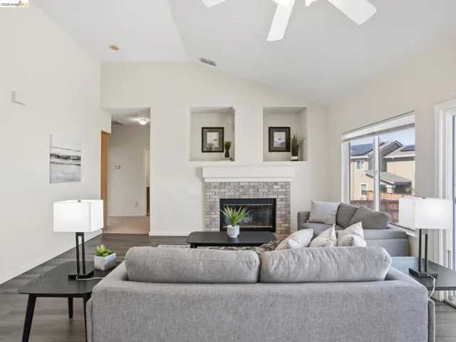 Living room featuring vaulted ceilings, wood-finish flooring, and a fireplace with a light-colored brick surround and mantel