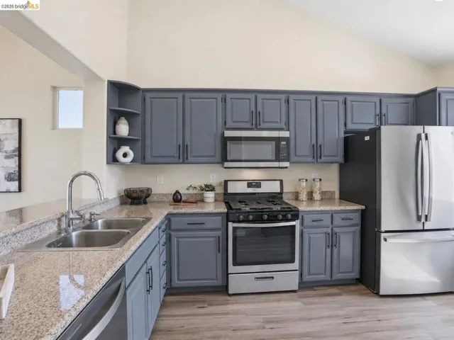 Kitchen featuring gray cabinetry, stainless steel appliances, granite countertops, and wood-finish flooring