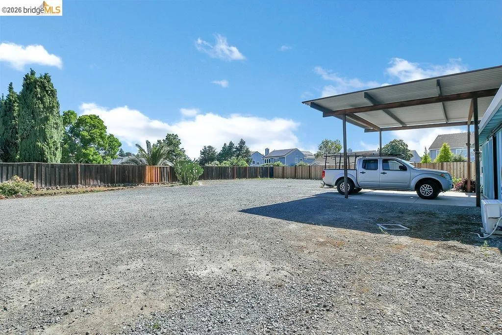 Expansive gravel-surfaced yard featuring a metal carport structure with a concrete pad