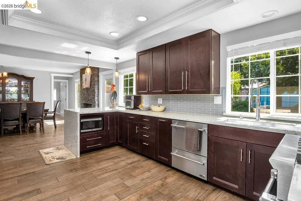 Kitchen featuring wood-finish flooring, dark wood cabinetry, light countertops, a subway tile backsplash, and stainless steel appliances