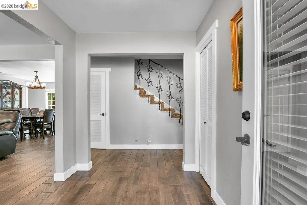 Entryway featuring wood-finish flooring, a staircase with wrought iron balusters, white louvered bifold doors, and a paneled entry door with integrated blinds