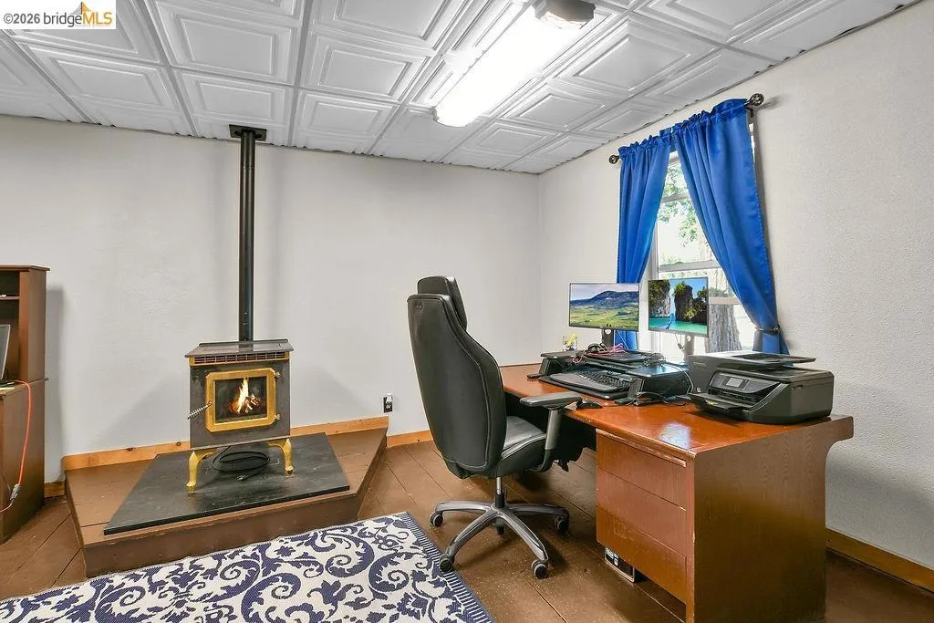Room featuring a freestanding wood-burning stove with a hearth, wood-finish flooring, and a decorative ceiling