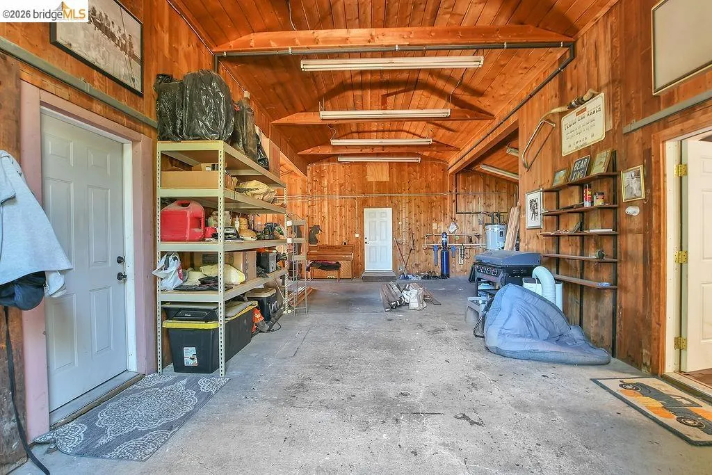 Spacious utility building with wood paneling, exposed wood beams, concrete flooring, and multiple entry points
