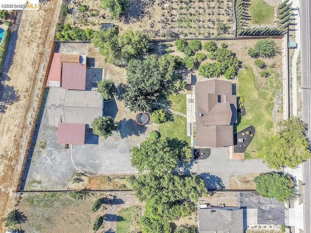 Expansive property featuring a main residence with a brown shingle roof, surrounded by mature trees and landscaped areas