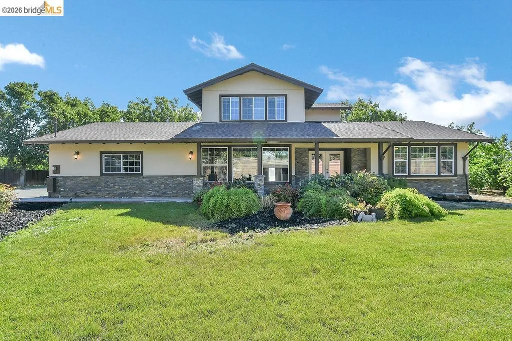 Contemporary home featuring an expansive front lawn, stone veneer accents, multiple large windows, a covered entry porch, and mature landscaping