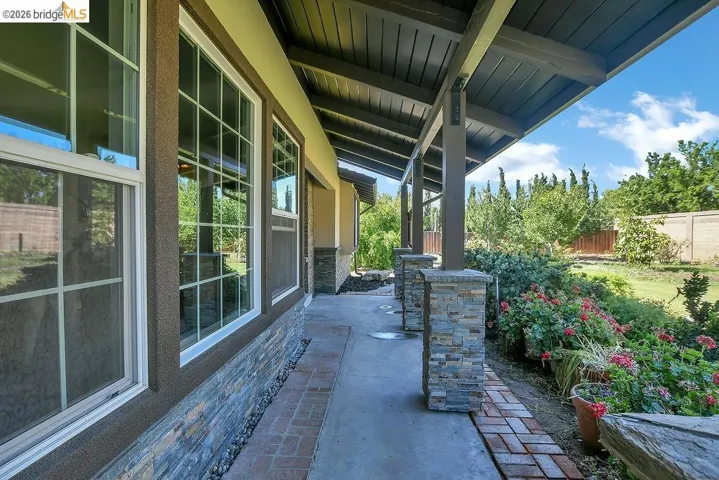 Covered patio with exposed wood beams, stone veneer columns, and a concrete walkway
