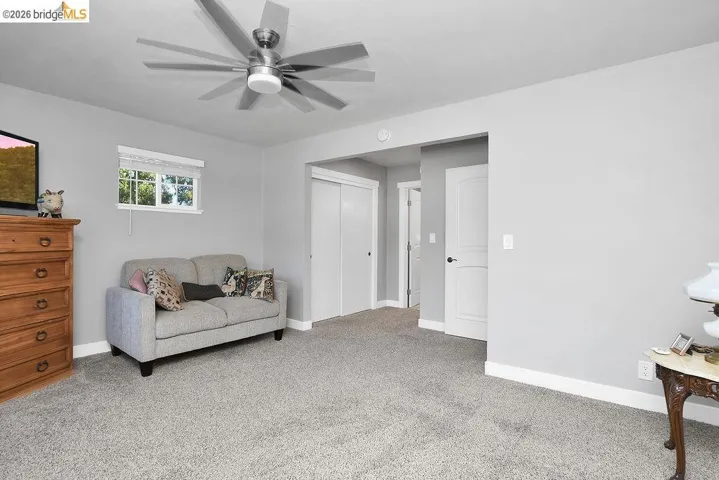 Spacious room featuring light gray walls, plush gray carpeting, a large ceiling fan, and white baseboards