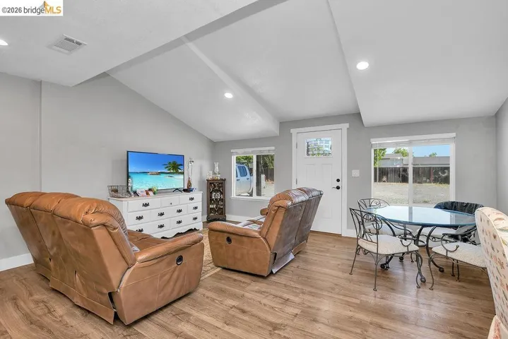 Open concept living area featuring vaulted ceilings with recessed lighting, wood-finish flooring, and multiple windows providing natural light