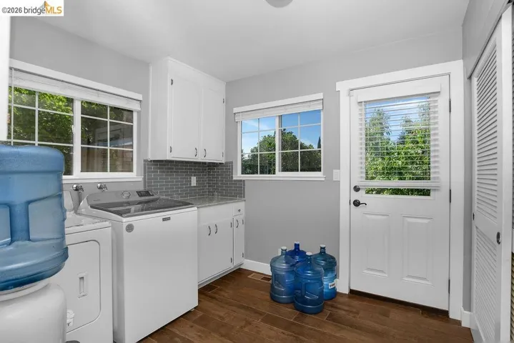 Laundry room featuring wood-finish flooring, white cabinetry, and a grey tile backsplash