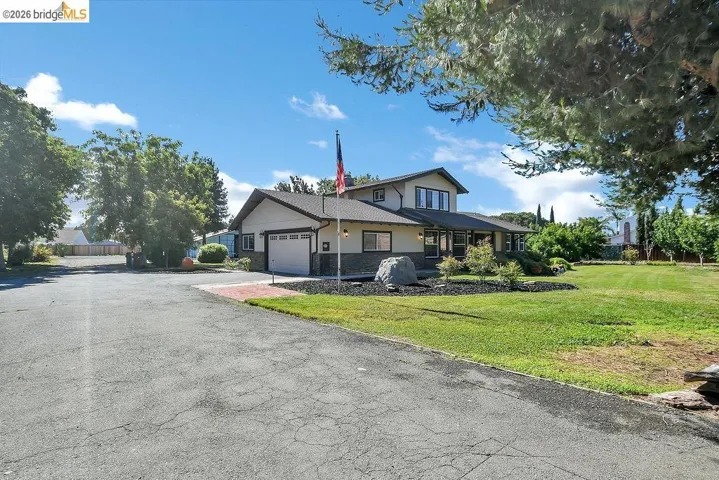 Two-story residence featuring a stone and stucco exterior, an attached garage, a covered front porch, and a flagpole