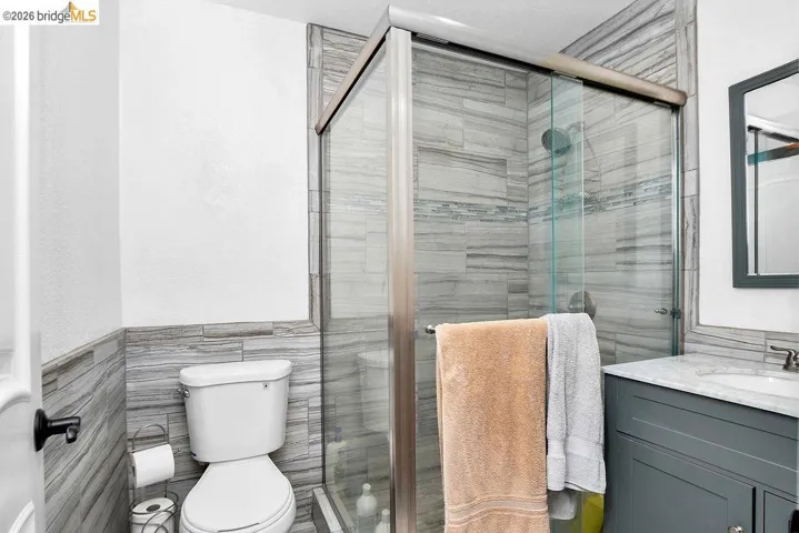 Bathroom featuring a sliding glass shower enclosure, gray wood-look tile, a single vanity with a white countertop, and a contemporary mirror