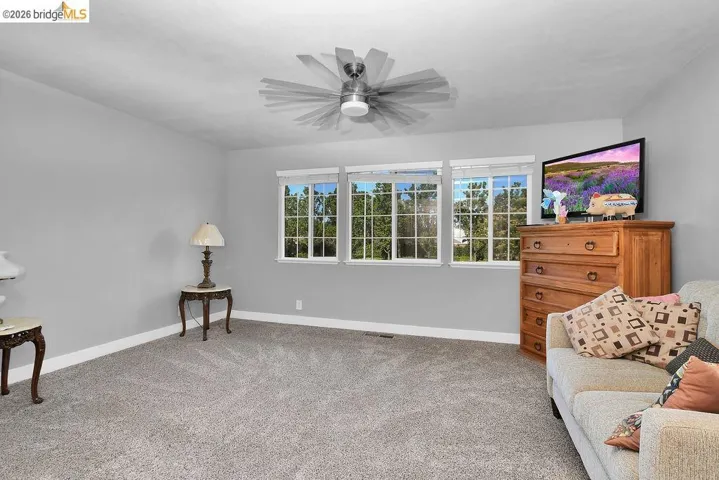 Expansive room featuring light gray wall paint, textured carpeting, and a modern ceiling fan