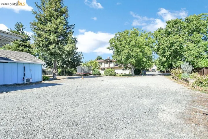 Expansive gravel lot featuring a light blue outbuilding with a dark shingle roof and an external HVAC unit