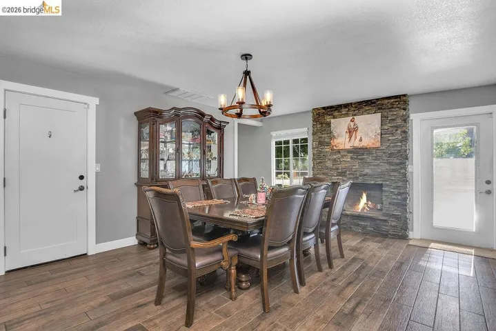 Dining area featuring wood-finish flooring, a stacked stone fireplace, and a wood-and-metal chandelier