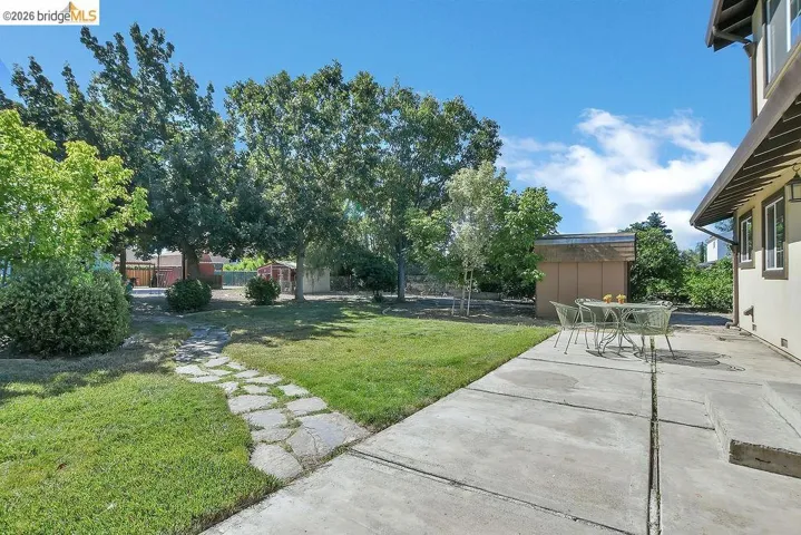 Expansive backyard featuring a concrete patio, a flagstone path, mature trees, and a storage shed