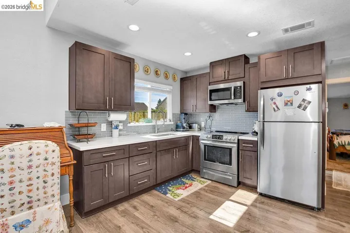 Contemporary kitchen featuring dark wood-finish cabinetry, stainless steel appliances, light countertops, a subway tile backsplash, and recessed lighting
