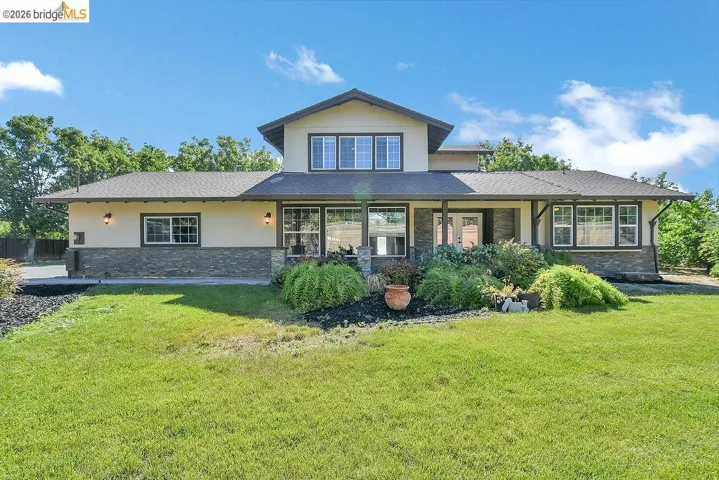 Contemporary home featuring an expansive front lawn, stone veneer accents, multiple large windows, a covered entry porch, and mature landscaping