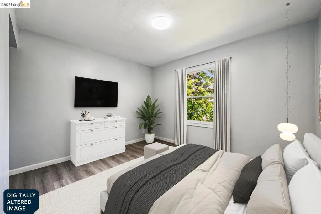 Spacious room featuring wood-finish flooring, a large window with natural light, modern ceiling light fixture, and light gray wall tones