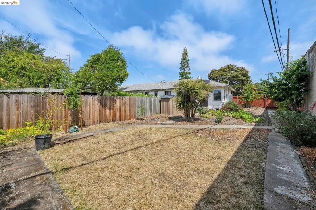 Spacious backyard featuring a wooden privacy fence, established shrubbery, and a concrete pathway
