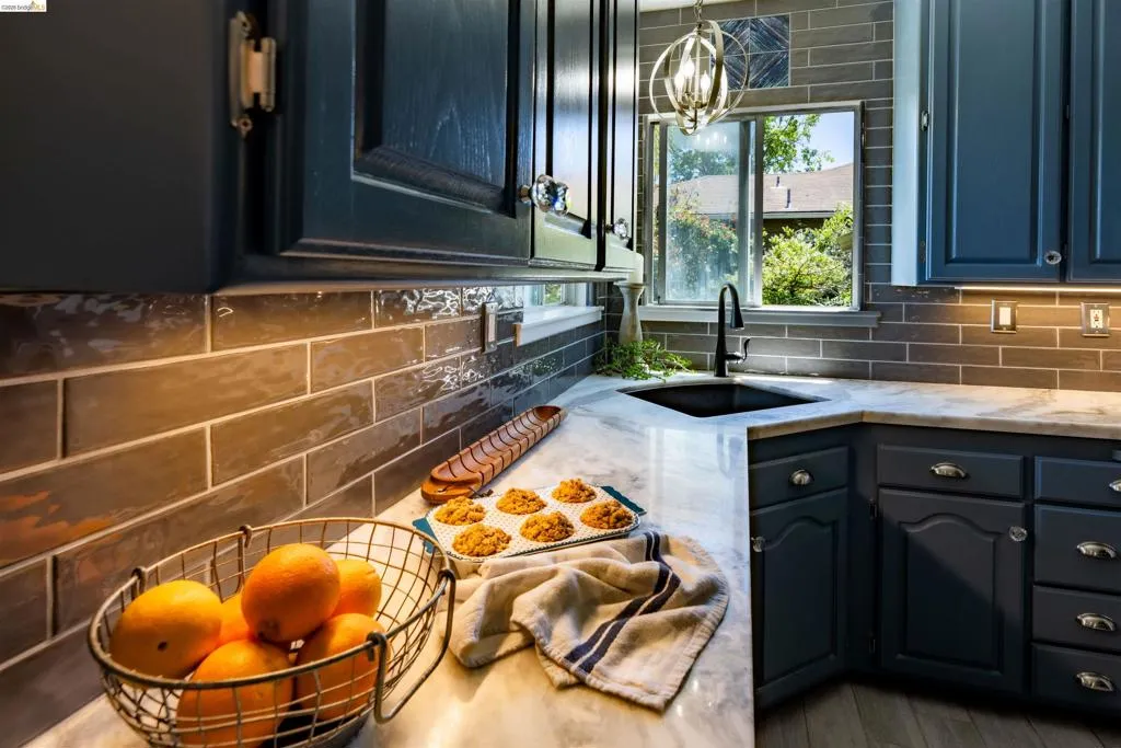 Kitchen featuring dark blue cabinetry with silver hardware, marble countertops, a black undermount Blanco Anthracite Diamond (25" x22") sink, a matching touchless gooseneck faucet, and a Blanco grid sink rack