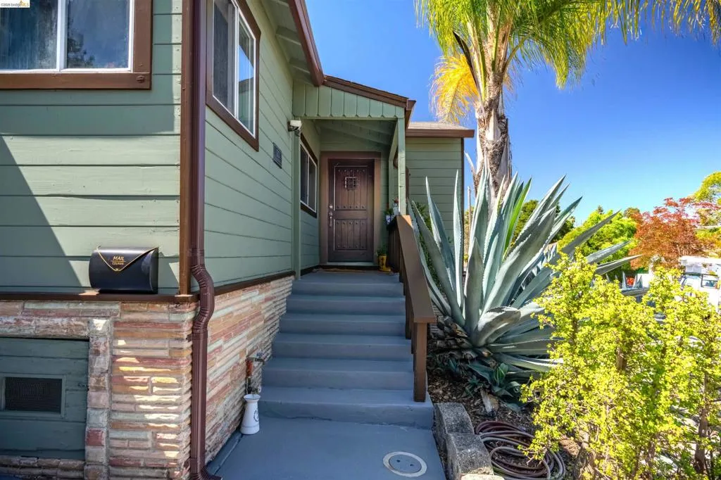Green horizontal siding with brown trim, featuring a brick foundation and a carved wood entry door
