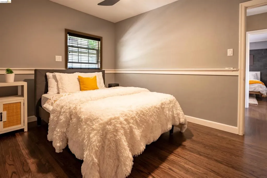 Bedroom 2 featuring wood-finish flooring, neutral wall tones, white baseboards, a window with blinds, and walk-in closet
