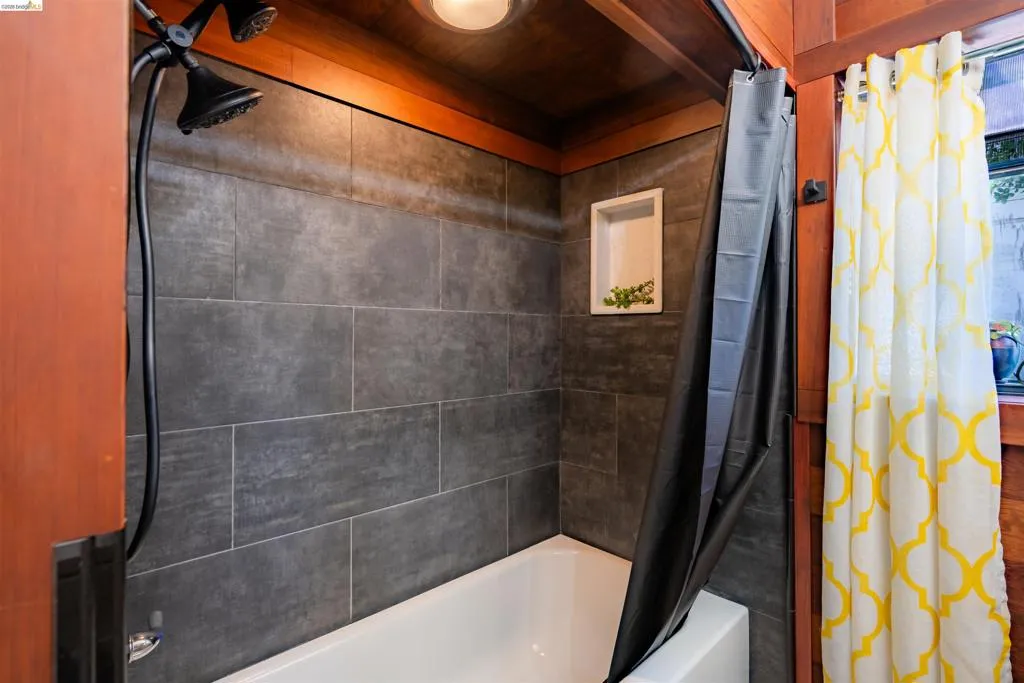 White bathtub featuring dark gray rectangular wall tiling and a built-in shower niche