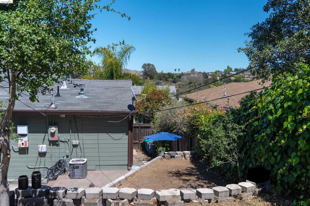 View from the top of the steps at the garage door entrance. Terraced backyard with retaining wall, mature trees, and foliage