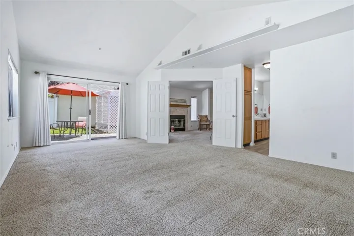 Primary suite with double doors to living space, large sliding door access to side yard, vaulted ceilings, natural light, and large en suite bathroom