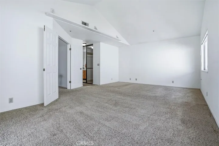Primary bedroom with vaulted ceilings, clean carpet, and en-suite bathroom