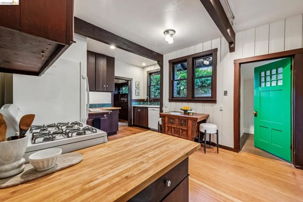 Kitchen featuring wood-finish flooring, wood beam accents, white paneled walls, dark wood cabinetry, and a butcher block countertop island