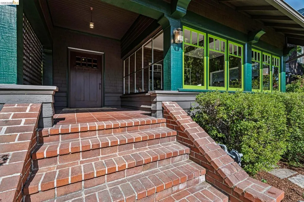 Brick entry stairs and landing lead to a covered porch with a gorgeous wood entry door and allow a glimpse into the enclosed sun porch!