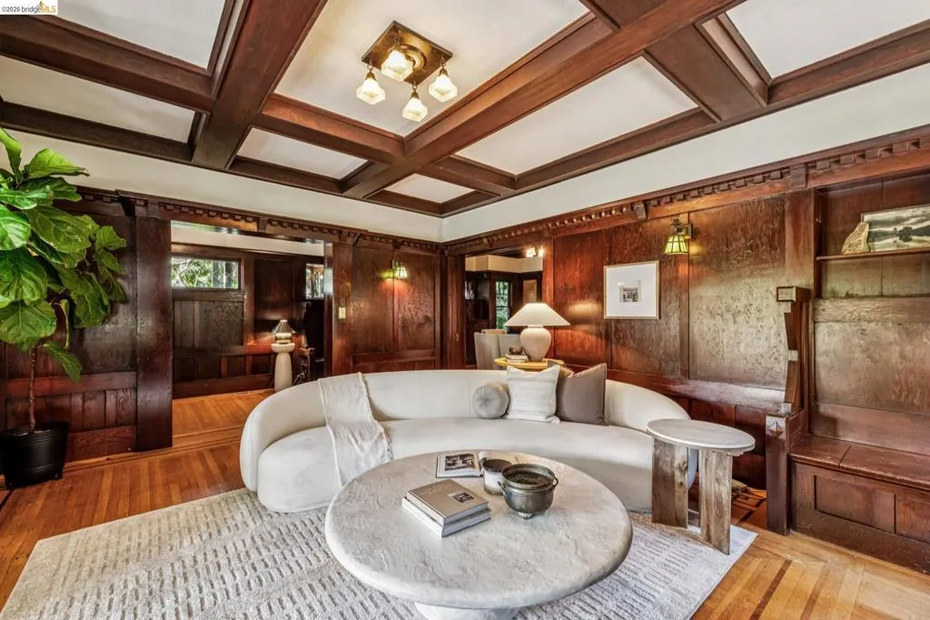 Living space featuring rich wood paneling, oak with walnut inlay flooring, a coffered ceiling, and built-in shelving and incredible cornice details