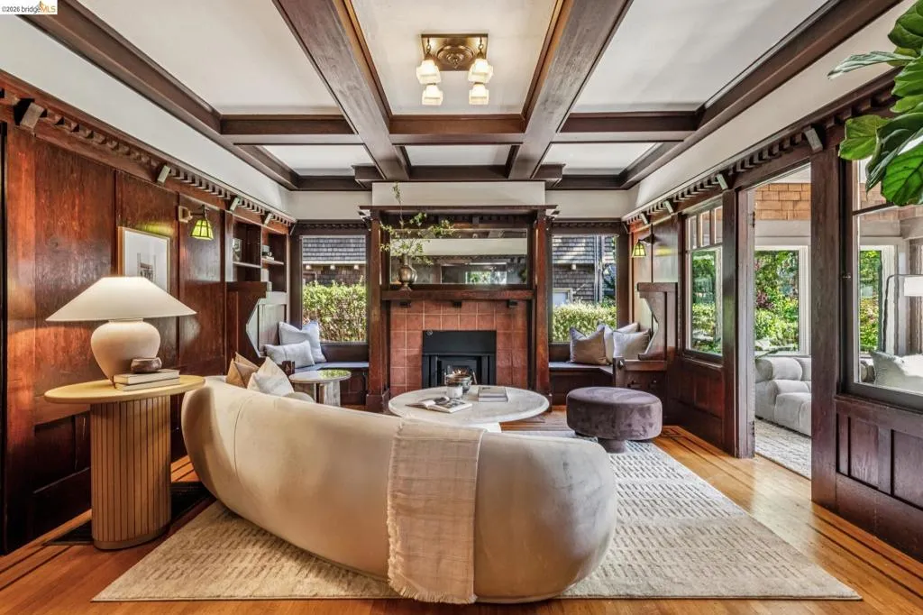 Feel the history in this gorgeous living room featuring rich wood paneling, coffered ceilings, a fireplace with a tile surround, built-in window seating, and hardwood flooring with walnut inlay.