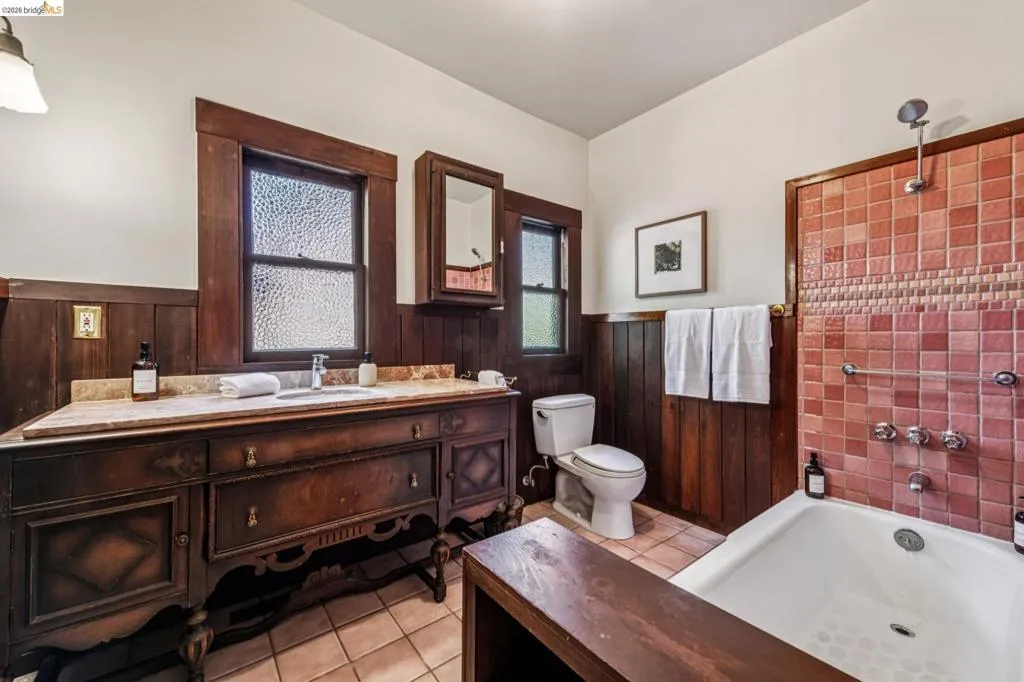 Bathroom featuring a red tiled shower surround, dark wood wainscoting, and a stone-topped vanity.
