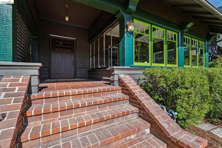 Brick entry stairs and landing lead to a covered porch with a gorgeous wood entry door and allow a glimpse into the enclosed sun porch!