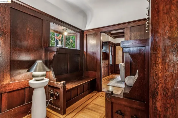 Stunning wood-paneled entryway featuring an integrated built-in bench, an open archway, a decorative wood-finish floor pattern, and a window providing natural light